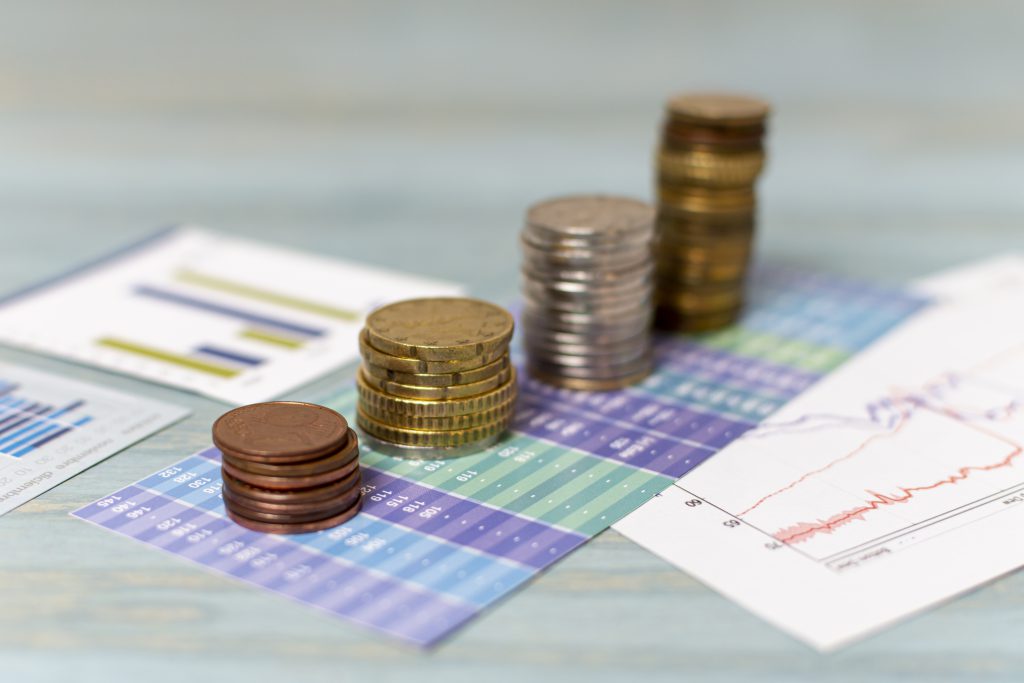 Zbliżenie na stosy monet obok wykresów finansowych i raportów, symbolizujących fundusze inwestycyjne na rynku kapitałowym