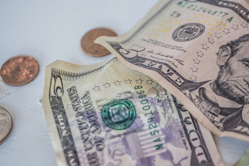 Zbliżenie na banknot pięciu dolarów oraz monety leżące na jasnej powierzchni jako symbol finansów i płatności.